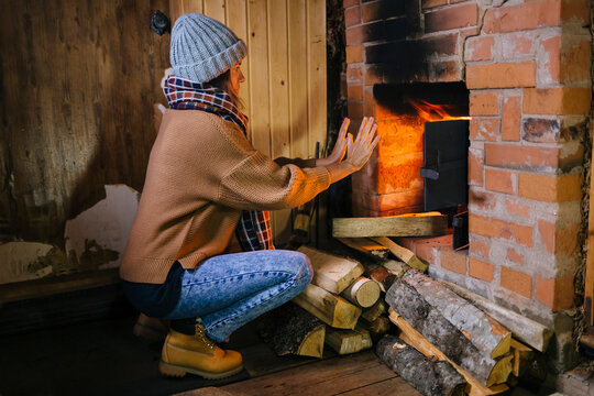 Woman crouching in front of fireplace warming her hands