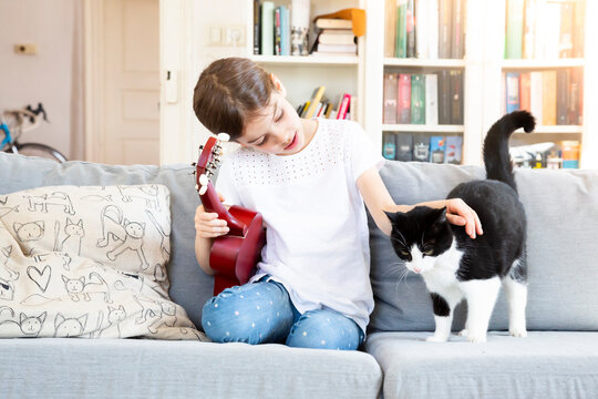 Girl with ukulele sitting on couch stroking cat