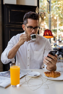 Businessman having breakfast in a cafe and checking cell phone