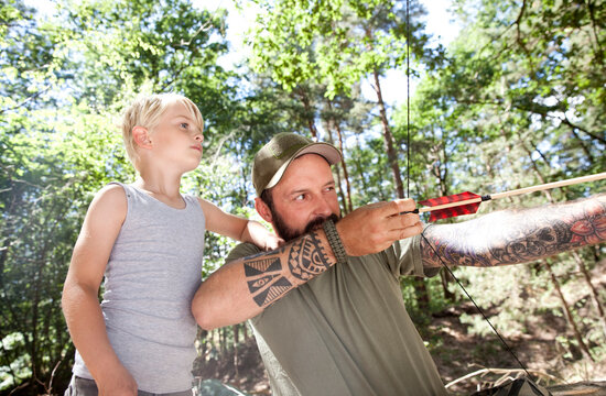 Son watching father shooting with bow and arrow in the forest