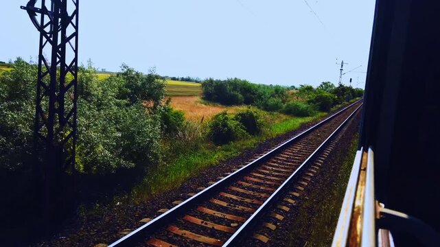 Professional POV footage from a moving train window looking out at the tracks and lush green fields of Hungary. A scenic and rhythmic rail journey through the European countryside in summer.