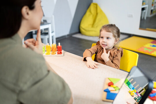Speech therapist working with a young girl on articulation and developmental skills, performing logopedic exercises during an educational session