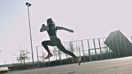 Fototapeta premium A young athlete mid-jump on an urban track, dynamic movement and athletic prowess. Worm's-eye view, clear sky, modern lighting. Captures sport training and city life, dedication, and fitness.