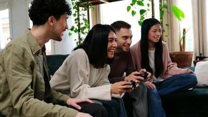 Four diverse young adults playing video games together, smiling and laughing in a living room © Ladanifer