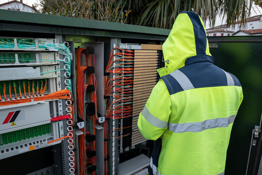 T&eacute;cnico especialista em telecomunica&ccedil;&otilde;es com casaco de alta visibilidade a realizar manuten&ccedil;&atilde;o e repara&ccedil;&atilde;o de avaria de fibra &oacute;tica num arm&aacute;rio de distribui&ccedil;&atilde;o