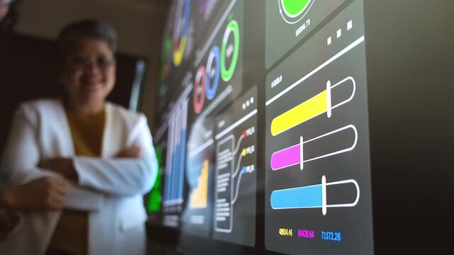 Hands point at colorful data sliders and charts on a large interactive dashboard, while a colleague smiles in the background during a data analytics presentation.