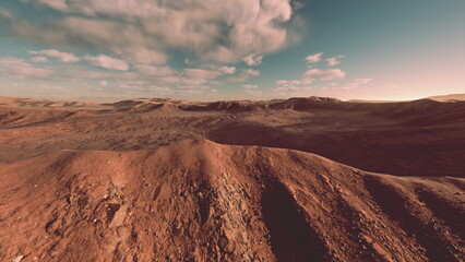 A stunning panorama showcases a rugged terrain bathed in warm tones as the sun begins to set. Clouds drift lazily above, casting shadows across the undulating hills, creating a serene atmosphere. © icetray