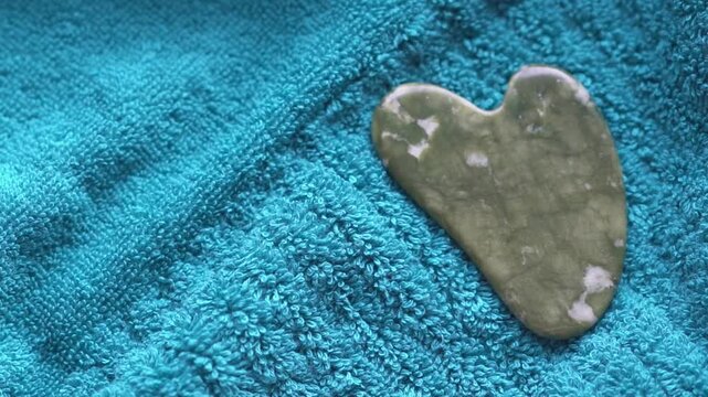 Guasha scraper made of natural serpentinite stone tool with soft towel, close-up