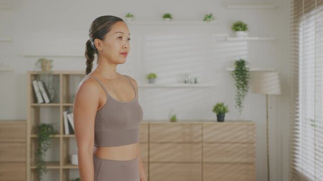 Focused Asian Woman  meditation and stretching at home living room fitness wellness routine, calm morning mindful breathing, raised arms standing pose in bright interior at home meditation