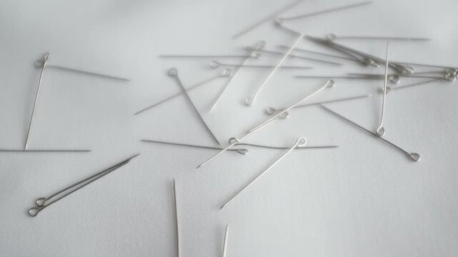 Professional-grade silver metallic sewing pins scattered on a clean surface. These fine-gauge steel dressmaker pins are for tailoring, delicate fabric draping, and high-fashion garment construction