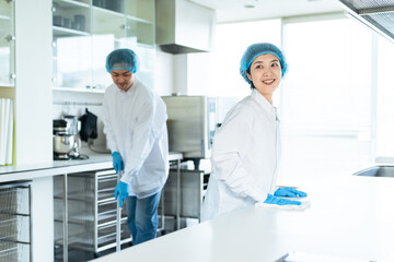 Obraz premium 厨房を清掃する衛生白衣を着た男女スタッフ