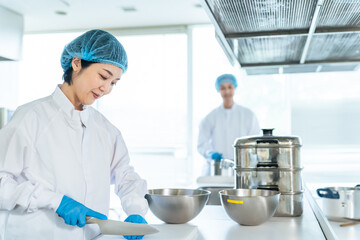 調理師、厨房、キッチン、給食センター、食品、工場、加工、チームワーク、笑顔、日本人、食堂、飲食店、バックヤード、同僚、女性、男性、衛生、白衣、作業員、惣菜、スーパーマーケット、食べ物、包丁、カット、調理器具、台所、宅食、給食室、学食、社食、おばさん、ミドルエイジ、キャップ、ヘアネット、手袋、清潔感、除菌、安全、業者、料理、働く、フード、職業、製造、室内、アルバイト、パート、仕事、人物 © metamorworks