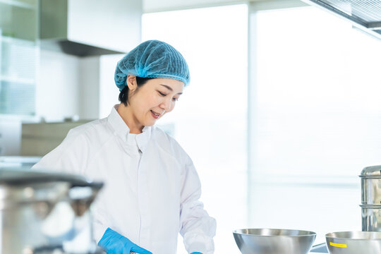 厨房で料理する衛生白衣を着た女性調理師　給食センター　給食室