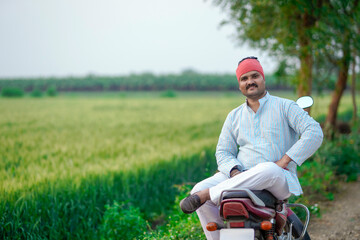 Fototapeta premium young indian farmer sitting on bike and gesturing with hand at field