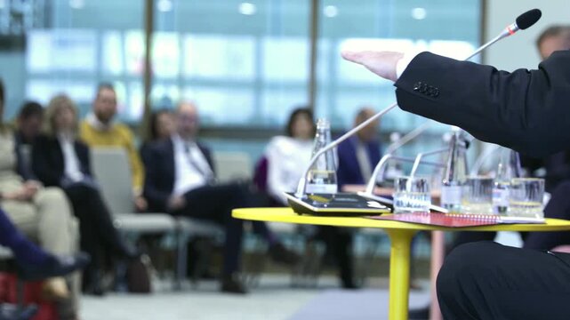 Business conference roundtable panel discussion with microphones and a blurred audience, featuring a professional corporate meeting interior during a seminar or workshop