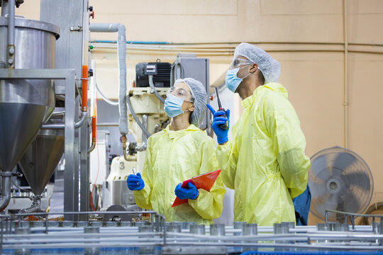 Technical team monitoring control panel and machinery at professional food production facility, Specialists in protective suits auditing safety and hygiene standards on industrial production line