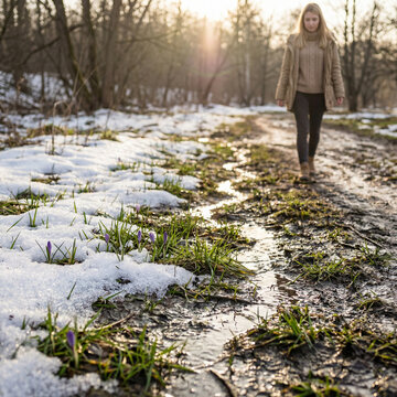 Early Spring Thaw Landscape with Fresh Green Grass Emerging Through Melting Snow and Woman in Background