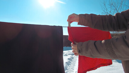 Hands hanging red laundry on a clothesline outdoors in winter with bright sun and blue sky background