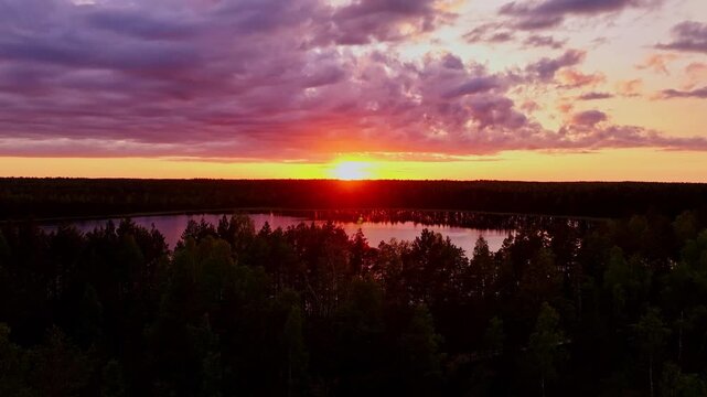 Glowing sunset paints clouds above calm bog lake surrounded by dark forest