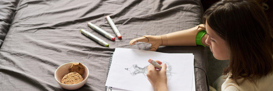 Girl with prosthesis drawing a sketch on a bed in a creative setting