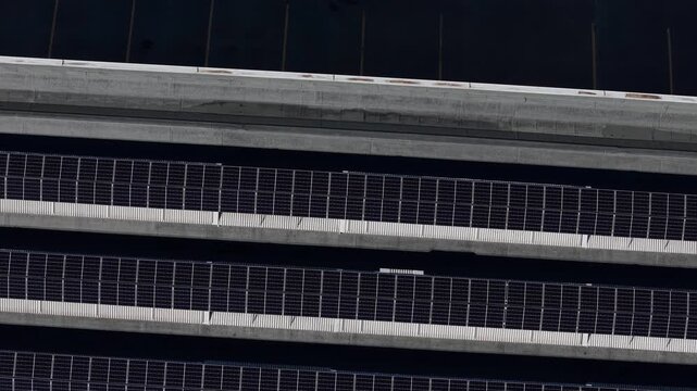 Photovoltaic solar panels installed in parallel rows on an industrial warehouse roof, emphasizing geometric lines, grid texture, and renewable electricity generation, drone top-down slow reveal.