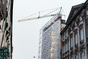 Fototapeta premium Urban construction scene featuring a historic building covered in scaffolding with a crane above, development and architectural transformation.