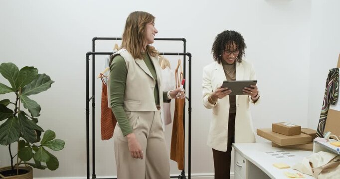 Diverse female designers exchanging ideas in studio, pinning swatches and tapping tablet for layout