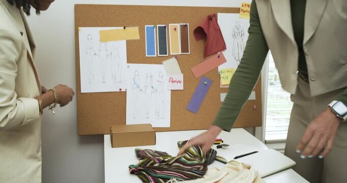 Comparing striped sample with sketches, Diverse female designers pinning it on cork board in studio