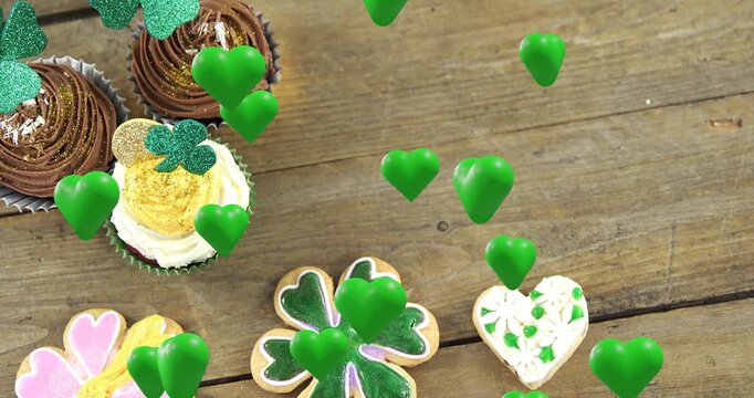 On play animated green hearts drifting over wooden tabletop, highlighting shamrock cupcake cluster