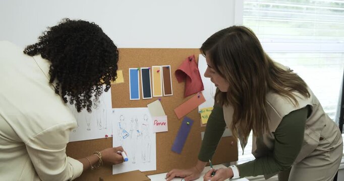 Two designers starting work at white table pinning sketch and arranging swatches to finalize layout