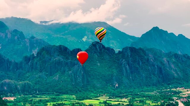 Colorful Hot Air Balloons Flying Over Lush Green Valley and Mountain Range on a Bright Day At Vang Vieng Laos PDR