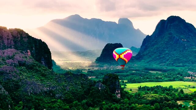 Colorful hot air balloon floating above lush green valley surrounded by majestic mountains at Vang Vieng Laos PDR