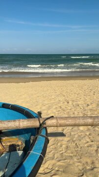 Traditional blue basket boat resting on golden sand, facing the calm ocean and horizontal water line, representing coastal livelihoods, travel, and serene beach atmosphere under a clear sky