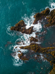 Obraz premium Drone view of powerful Atlantic Ocean waves crashing against rugged volcanic rocks along the dramatic coastline of Madeira Island, Portugal. 