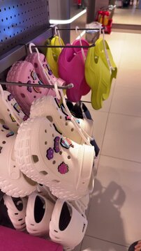 Customers hand selecting colorful rubber clogs with various cartoon charms from a display rack in a modern footwear store. Showcasing playful fashion choices and a variety of personalized accessories