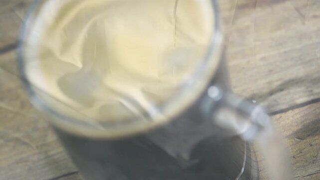 Cream pouring into dark coffee, swirling and spreading, forming smooth crema on glass mug