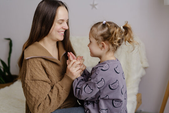 A woman and a girl sit together in a cozy room. They hold hands and play a hand-clapping game, sharing smiles and laughter in a joyful moment