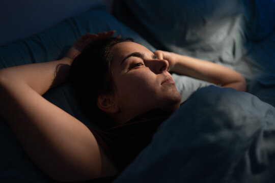 Close-up of woman face in night light. Girl drifts off sleep in her bed. Concept of insomnia, sleep disorder, poor rest and sleepless nights
