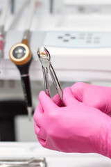 Dentist in pink gloves holds forceps with extracted tooth in clinical office.