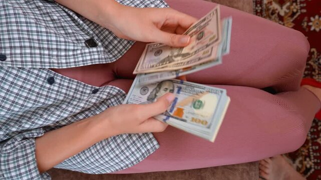 Top-down view of a woman sitting on a couch and quickly counting a large wad of American money, showing off her wealth, successful investments, or recent financial gains