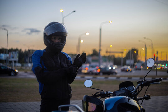A woman on a motorcycle wearing a helmet and a motorcycle jacket in the evening in the city