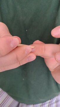 Close-up vertical video of woman pushing back cuticle with wooden orange stick during at-home manicure. Detailed hand care process, natural movement, DIY beauty routine and self care concept.