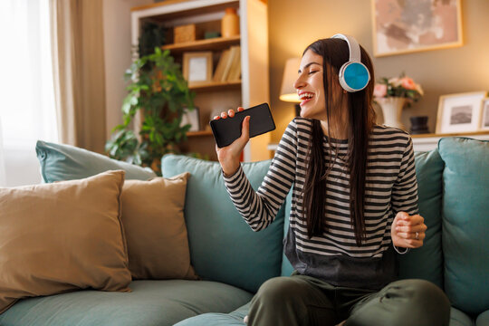 Woman wearing headset singing and dancing while listening to the music at home