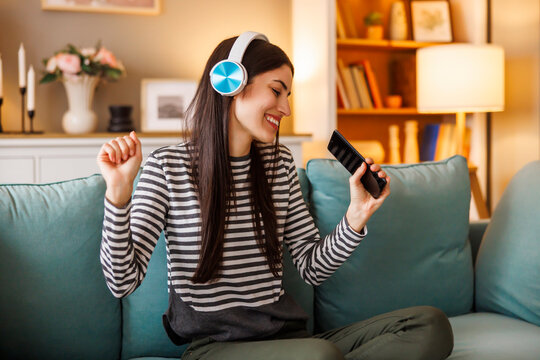 Woman wearing headset singing and dancing while listening to the music at home
