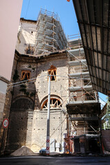 Naklejka premium Stone facade of an old building covered by scaffolding and a protective canopy during post earthquake restoration works along a narrow urban street in l Aquila Italy