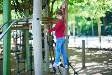 Obraz premium Little girl climbing playground equipment using ropes and platforms in a green city park