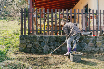 Young woman raking and preparing soil for planting in the backyard of her countryside house.