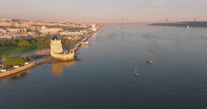 Bel&eacute;m Tower and anchored boats on Tagus River in Lisbon at golden hour, aerial drone medium wide shot, Portugal