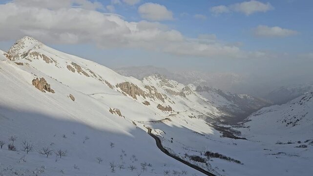 Breathtaking winter mountain valley: winding road snakes through deep snow-covered slopes under vast blue sky with scattered clouds and misty peaks.
📍Hawraman Takht, Kurdistan 