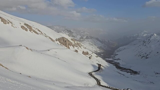 Breathtaking winter mountain valley: winding road snakes through deep snow-covered slopes under vast blue sky with scattered clouds and misty peaks.
📍Hawraman Takht, Kurdistan 